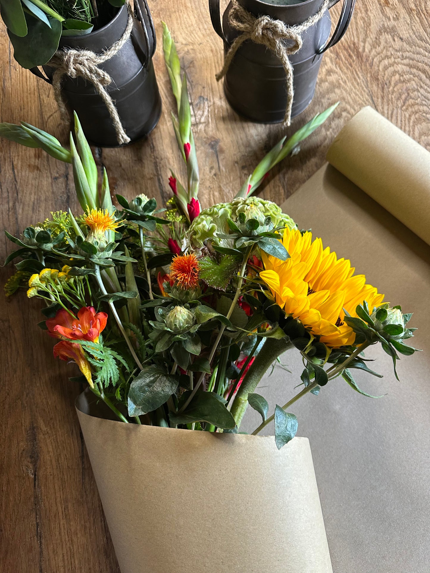 Bouquet of flowers in a paper bag on a wooden surface with two black lanterns in the background.