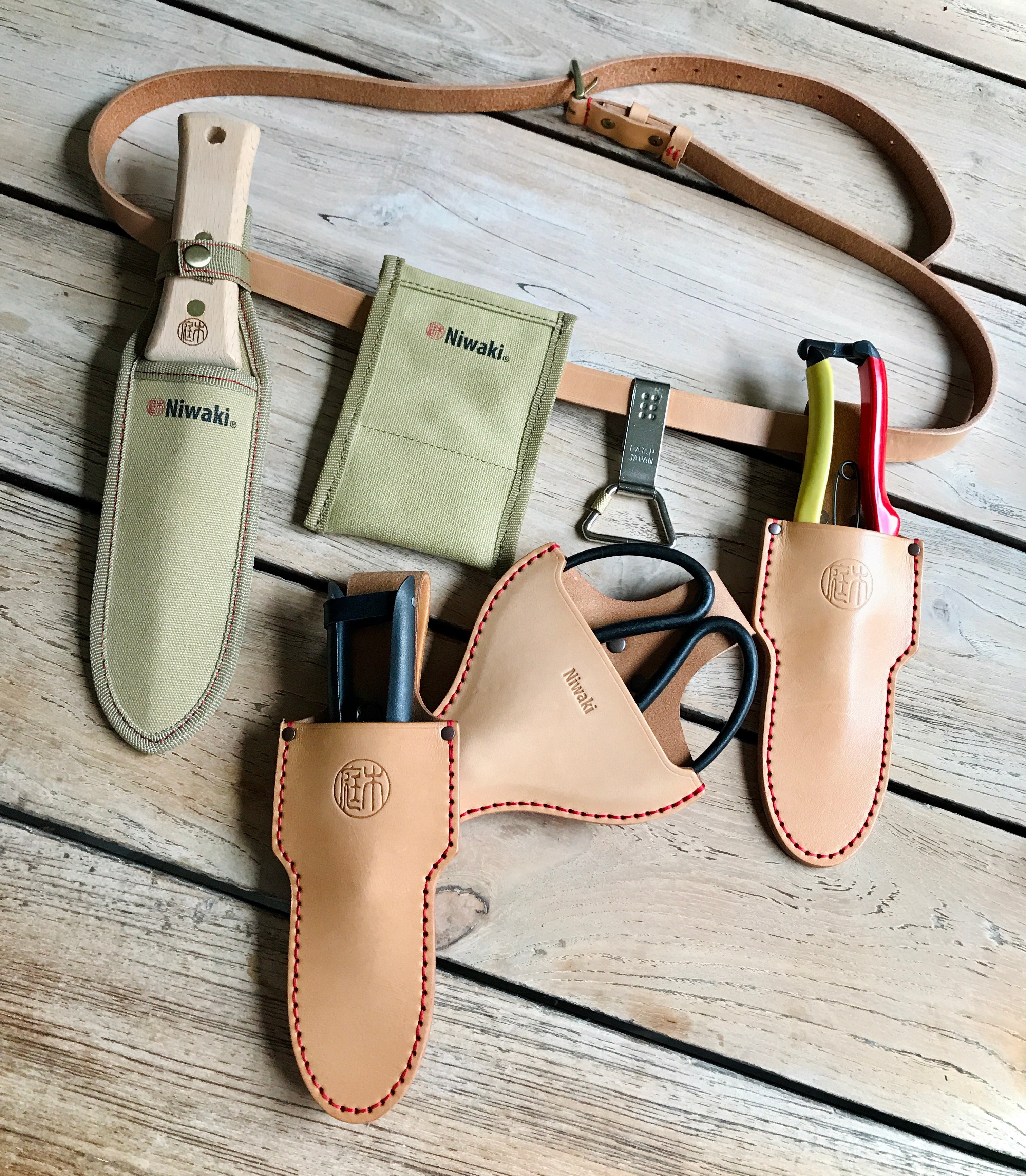 Niwaki gardening tools in a canvas tool bag resting on a Dartmoor stone wall, surrounded by oak trees and wild wall flowers on a sunny day