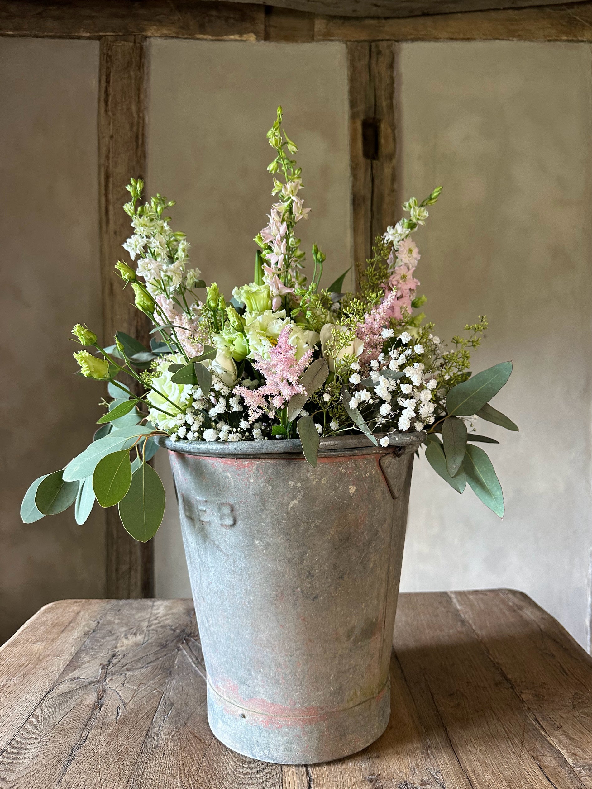 Floral arrangement in a metal bucket on a wooden table with a rustic background