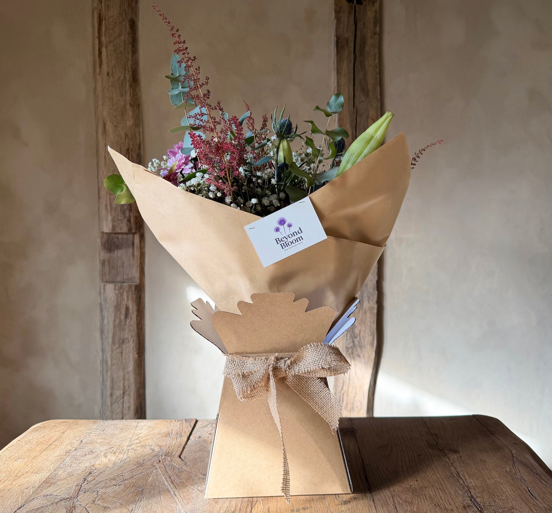 Bouquet of flowers wrapped in brown paper with a visible brand label on a wooden surface.