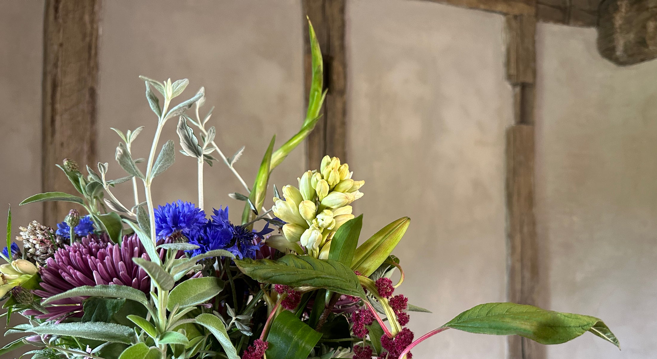 Colorful floral arrangement with greenery against a rustic wooden wall.
