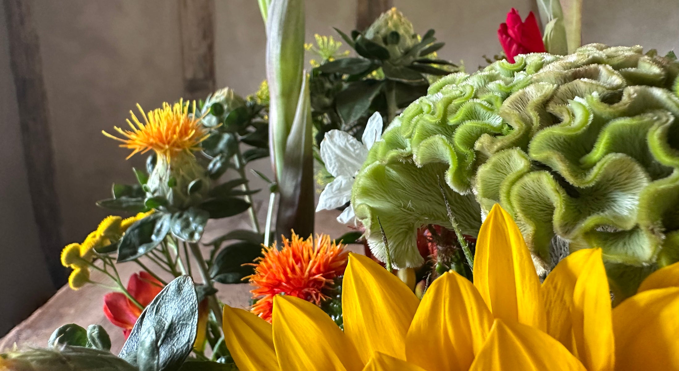Floral arrangement with yellow sunflowers, red flowers, and green foliage.