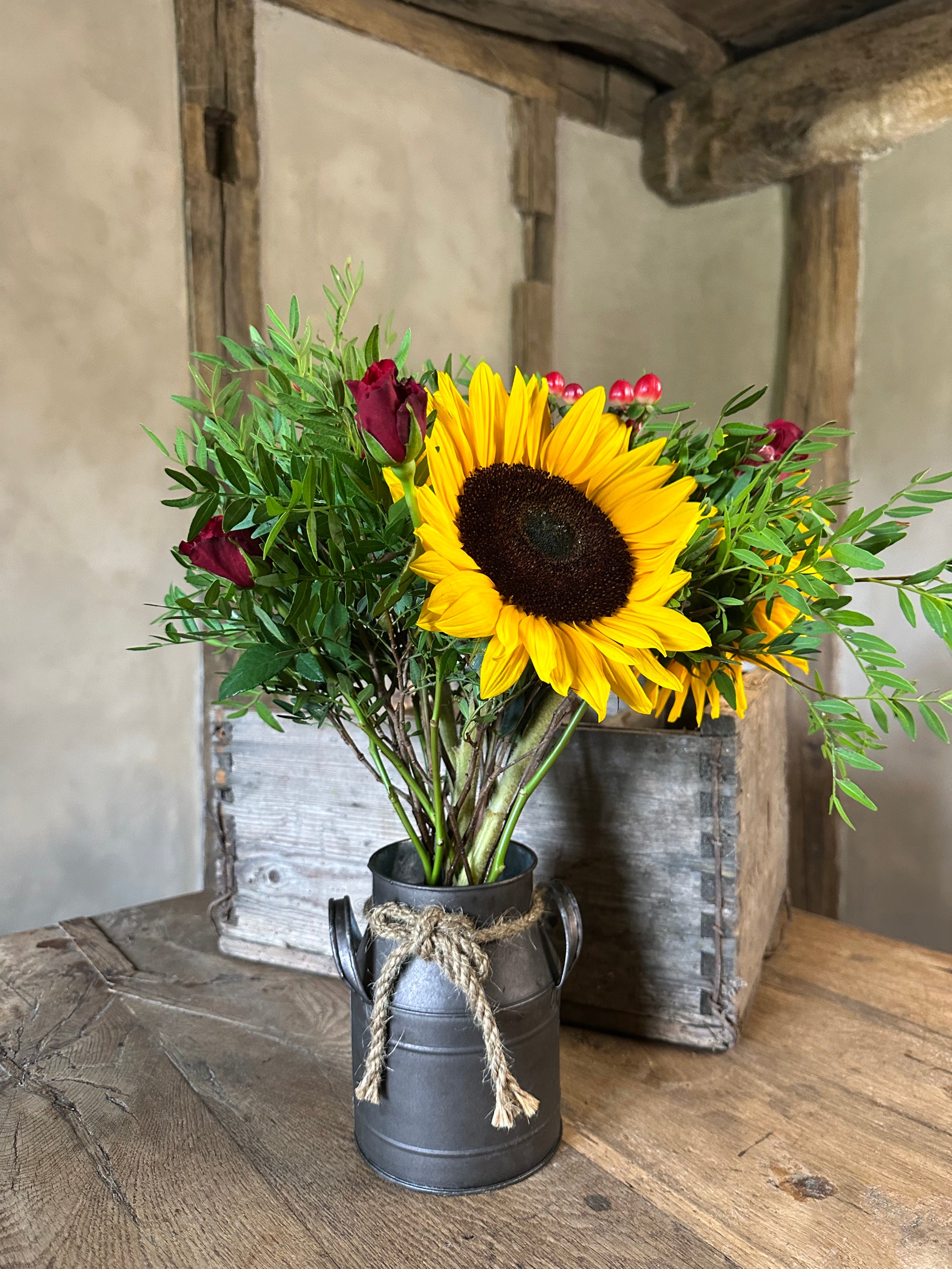 Sunflower arrangement in a black watering can on a wooden surface with rustic background